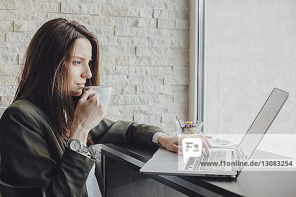 Seitenansicht einer Geschäftsfrau  die Kaffee trinkt  während sie ihren Laptop am Café-Tisch benutzt