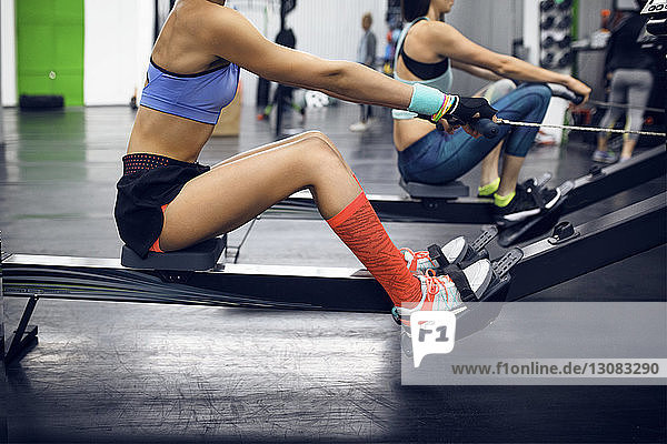 Seitenansicht von entschlossenen Sportlerinnen mit Rudergerät im Fitnessstudio