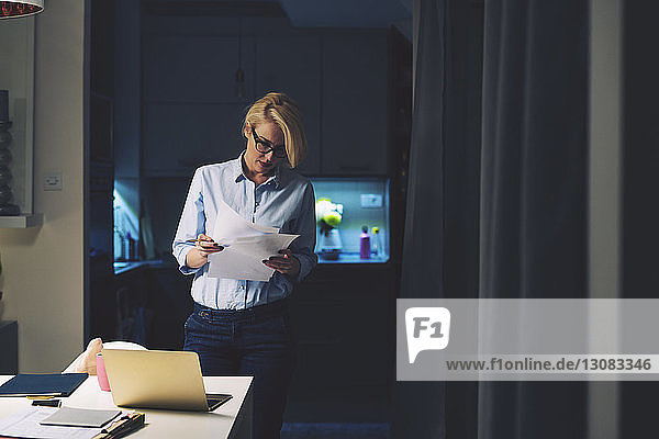 Businesswoman reading documents while standing by desk in home office