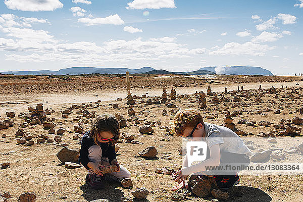 Siblings playing with rocks at desert during sunny day