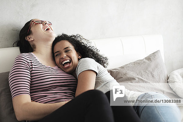 Happy lesbian couple laughing while relaxing on bed at home