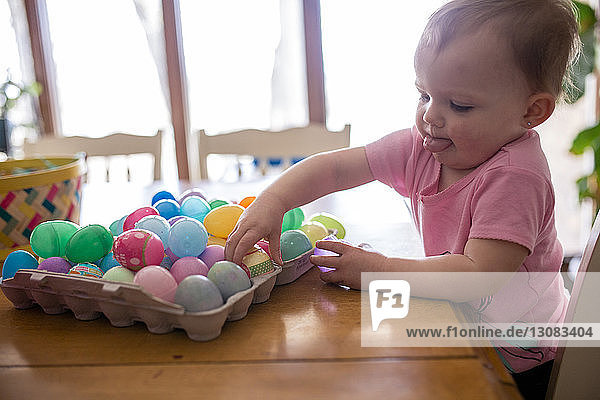 Süßes Mädchen spielt zu Hause auf dem Holztisch mit bunten Ostereiern