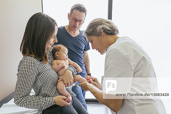 Female doctor examining baby boy with parents at hospital