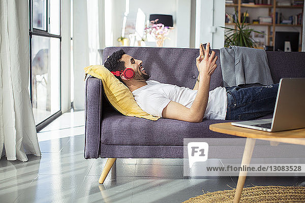 Happy businessman using tablet computer while lying on sofa in office