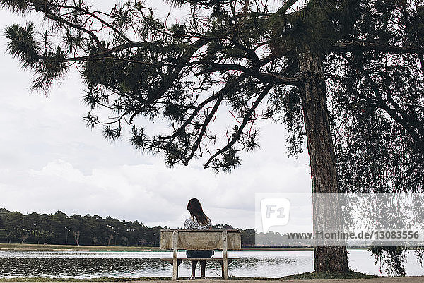 Frau in voller Länge auf Bank am See im Park sitzend