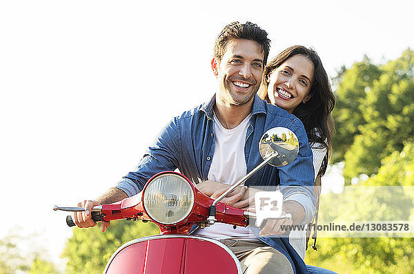 Glückliches Paar fährt auf einem Motorroller gegen den klaren Himmel