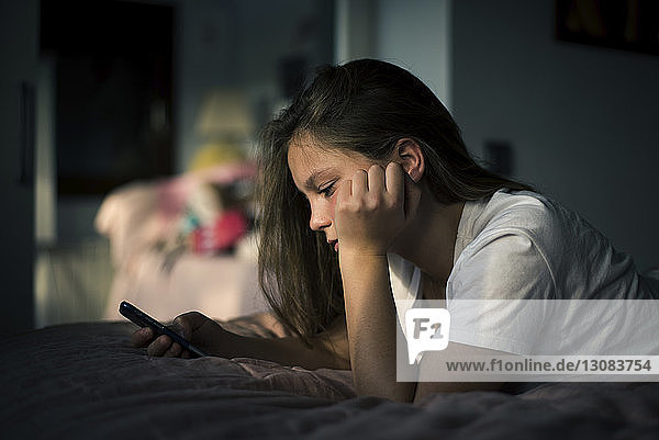 Teenager-Mädchen benutzt Smartphone  während sie zu Hause im Bett liegt