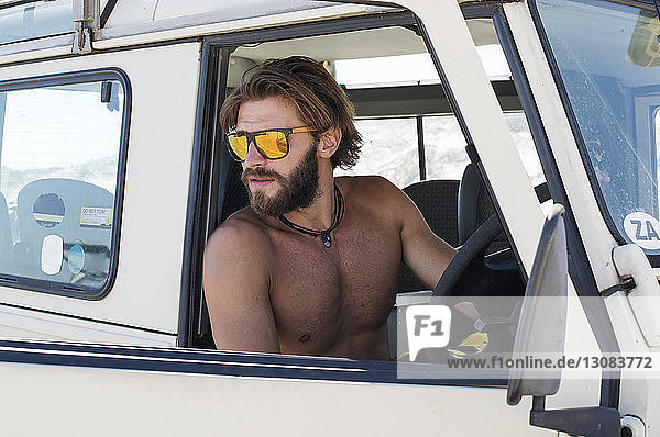 Shirtless man wearing sunglasses sitting in off-road vehicle