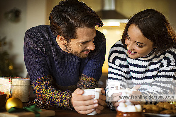 Smiling couple having coffee marshmallow at table during Christmas