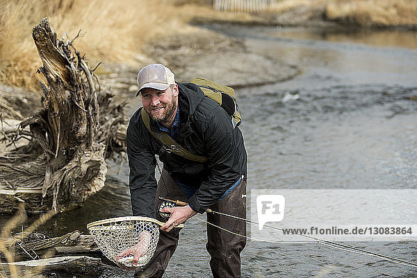 Smiling man removing fish from butterfly fishing net while standing in river