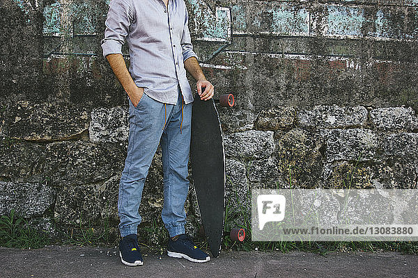Niedriger Abschnitt eines Mannes  der ein Skateboard hält  während er an der Wand steht