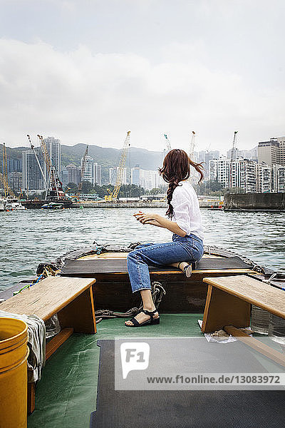 Seitenansicht einer Touristin  die in Hongkong auf einem Boot sitzt und Gebäude betrachtet