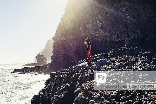 Side view of woman standing on rocky shore on sunny day