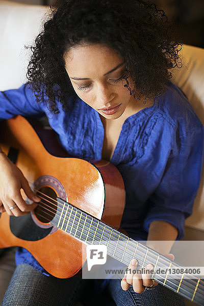 Hochwinkelansicht einer Frau  die auf dem Sofa sitzend Gitarre übt