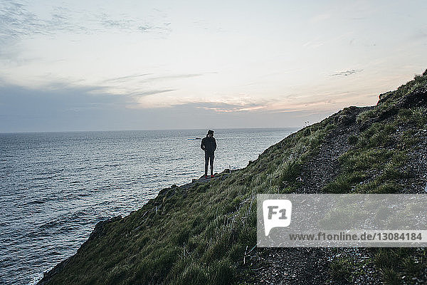 Hiker standing on mountain by sea against sky during sunset