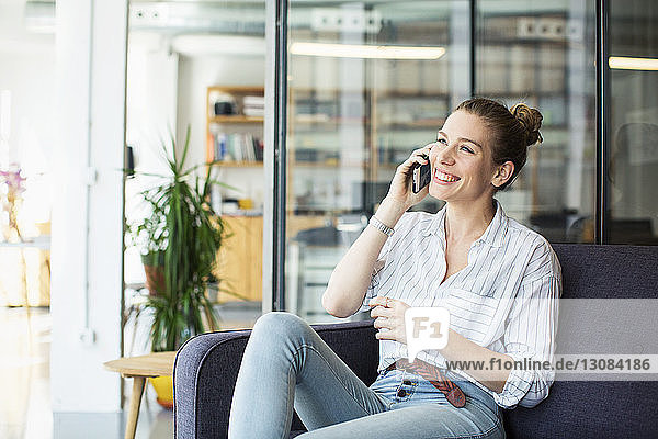 Glückliche Geschäftsfrau  die im Büro sitzt und mit dem Handy telefoniert