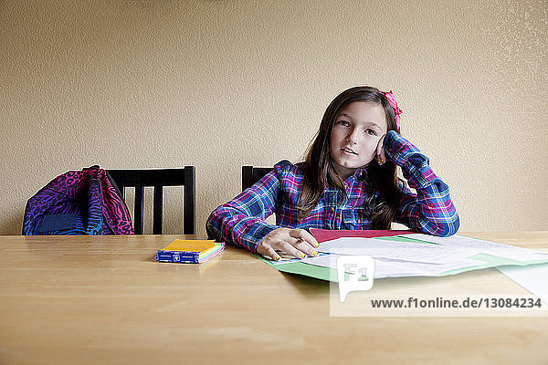 Porträt eines Mädchens  das lernt  während es zu Hause auf einem Tisch an der Wand sitzt