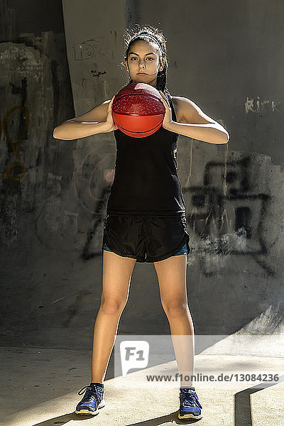 Porträt eines selbstbewussten Sportlers  der Basketball gegen die Wand hält