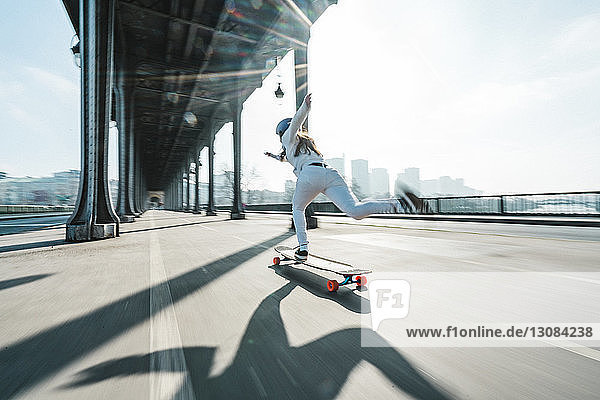Verschwommene Bewegung einer Frau beim Skateboarden unter einer Brücke in der Stadt gegen den Himmel