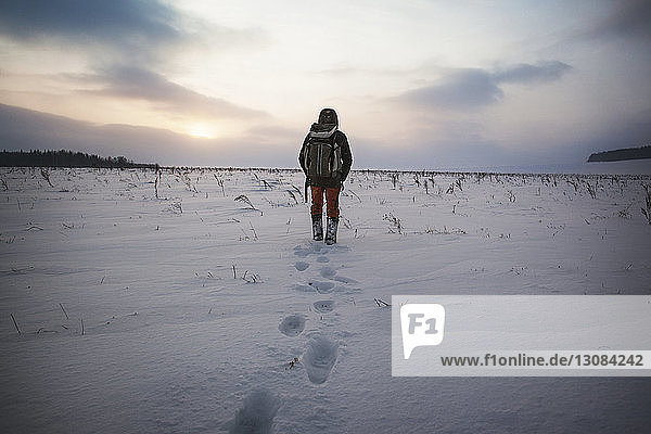 Rückansicht eines Mannes  der auf einem schneebedeckten Feld gegen den Himmel läuft