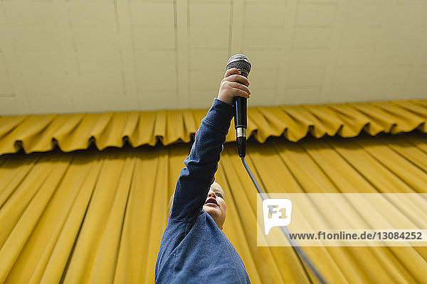 Niedrigwinkelansicht eines Jungen  der das Mikrofon auf der Bühne gegen gelbe Vorhänge hält