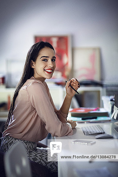 Porträt einer lächelnden Geschäftsfrau  die im Büro am Schreibtisch sitzt