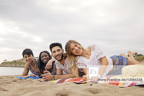 Portrait of cheerful friends lying on blanket at beach