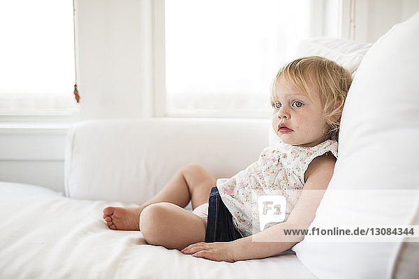 Girl looking away while relaxing on bed at home