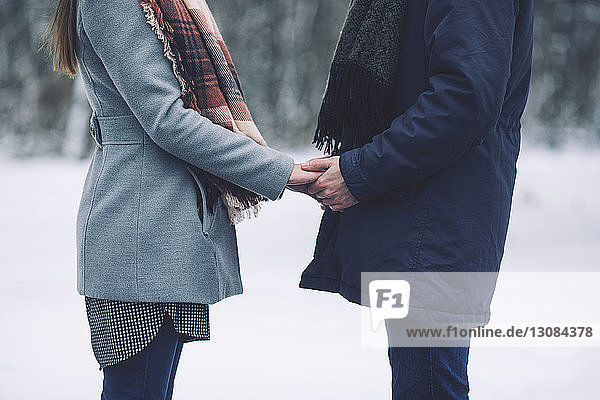 Midsection of couple holding hands while standing on snow covered field