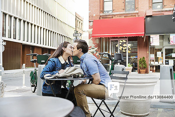 Pärchen küsst sich am Tisch im Straßencafé gegen Gebäude