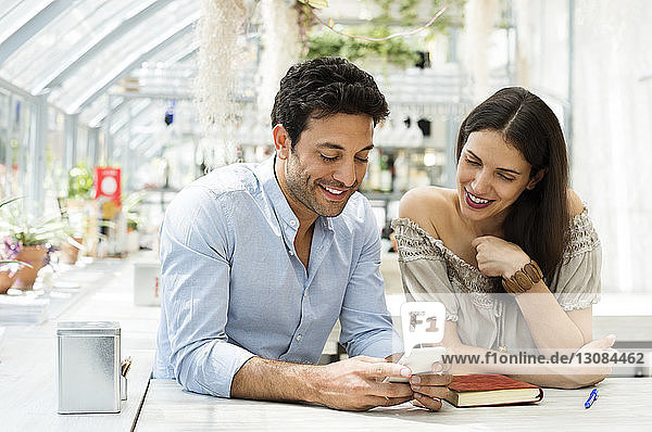 Smiling couple using smart phone at sidewalk cafe