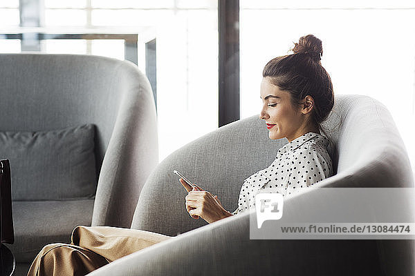 Seitenansicht einer Geschäftsfrau  die telefoniert  während sie im Restaurant auf dem Sofa sitzt