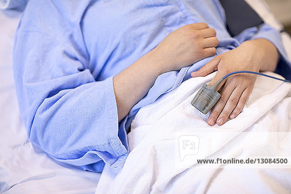 Midsection of female patient with pulse oximeter lying on bed in hospital