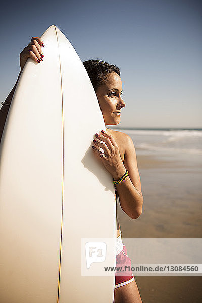 Thoughtful young woman standing with surfboard on beach