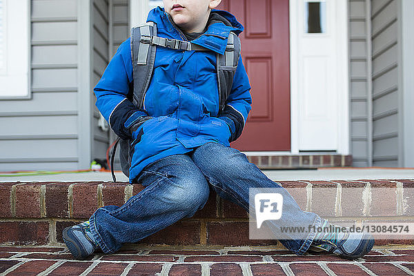 Low section of boy wearing warm clothing sitting in front of house