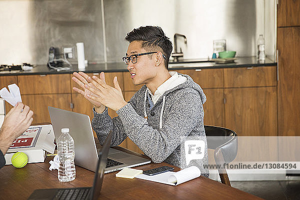Geschäftsmann mit Laptop-Computer gestikuliert  während er im Kreativbüro sitzt