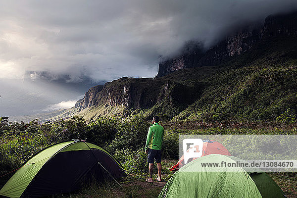 Rückansicht eines Mannes  der auf einem Campingplatz auf einem grünen Berg steht