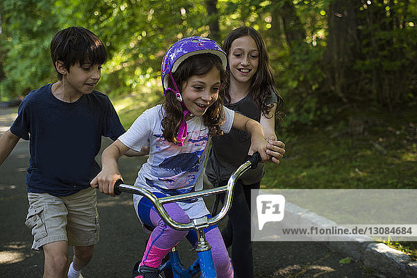 Geschwister unterstützen Schwester beim Fahrradfahren auf der Straße gegen Bäume im Park