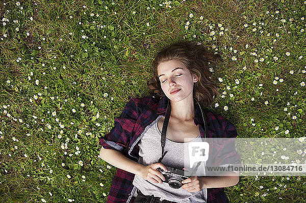 Overhead view of woman holding camera while lying on grass at park