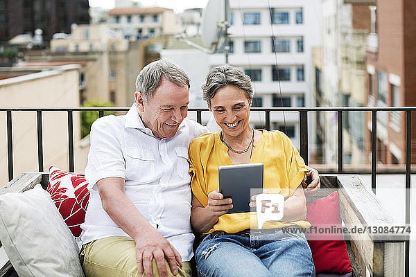 Fröhliches älteres Ehepaar benutzt Tablet-Computer  während es auf einer Bank auf der Terrasse sitzt