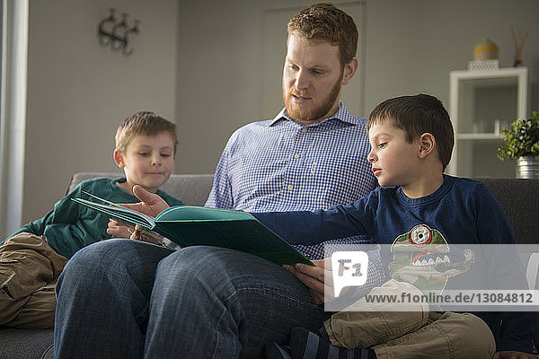 Father showing book to sons on sofa at home