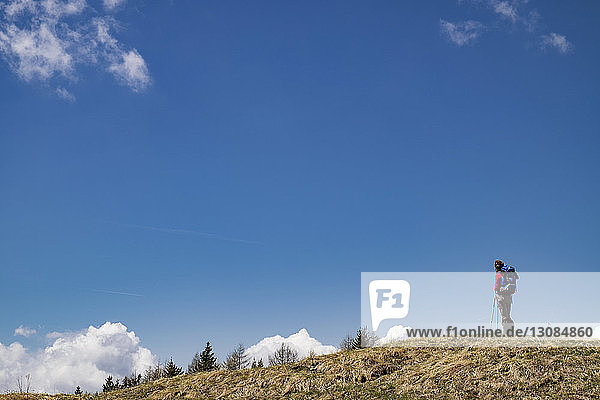 Low angle view of female hiker standing on mountain against blue sky