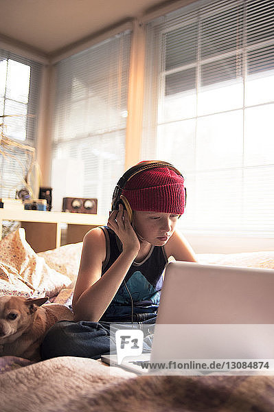 Junge hört Musik mit Kopfhörern  während er seinen Laptop im Bett benutzt