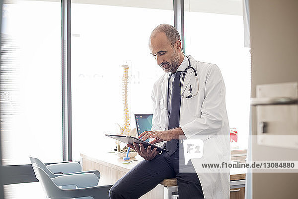 Arzt benutzt Tablet-Computer  während er im Krankenhaus am Schreibtisch sitzt