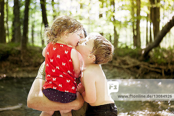 Bruder küsst Schwester  die vom Vater im Wald getragen wird