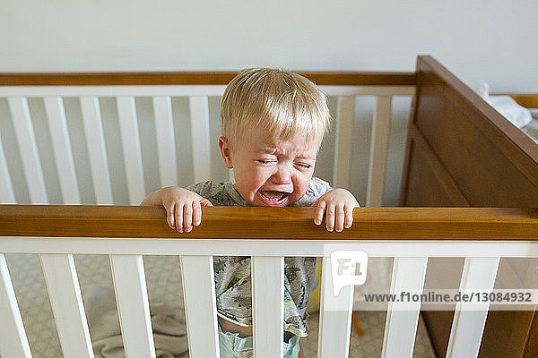 Kleiner Junge weint  während er zu Hause in der Krippe steht