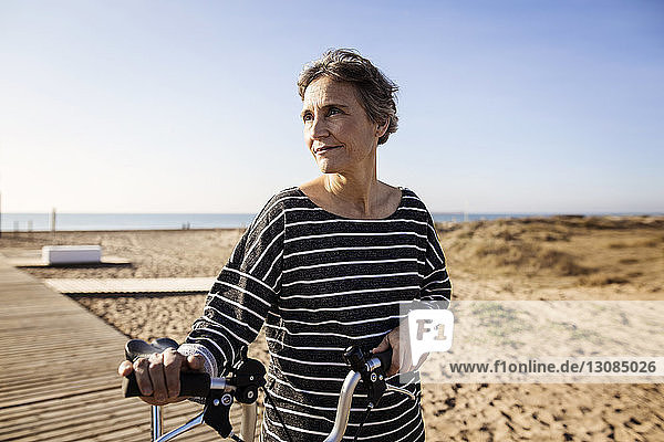 Frau mit Fahrrad am Strand vor klarem Himmel