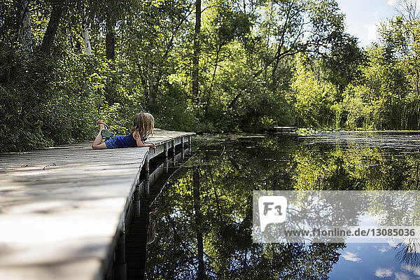 Side view of girl lying on pier by lake