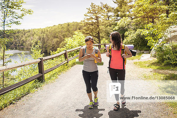 Woman looking at friend using smart phone while walking on road in forest