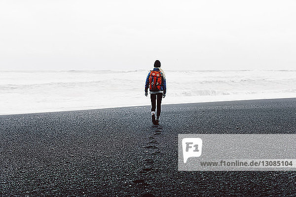 Rear view of woman walking on black sand beach against sky